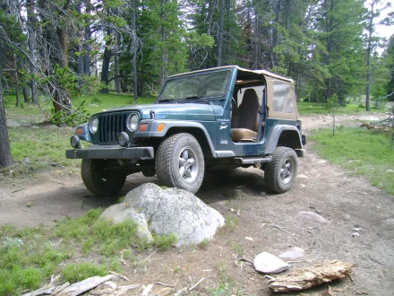 A Jeep Wrangler parked on a rugged trail among trees, showcasing its off-road capabilities. This high-definition image serves as a vibrant desktop wallpaper.