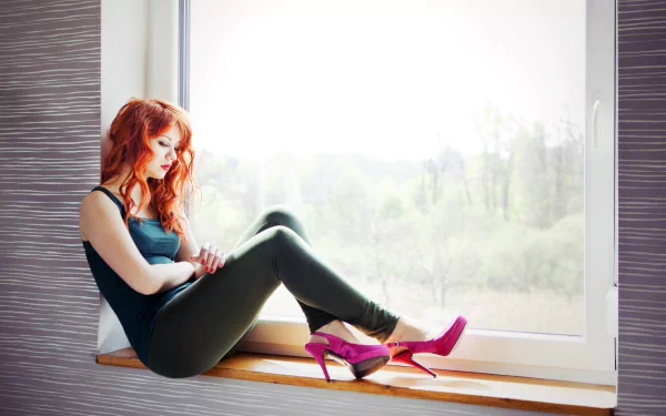A redheaded woman, wearing lipstick, sits on a windowsill, resting her arms on her legs. Pink high heels are displayed in front of her. This HD wallpaper showcases a serene, natural backdrop.