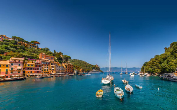 Vibrant colorful houses line the waterfront of Portofino, Italy, with boats floating on the crystal-clear ocean under a deep blue sky.