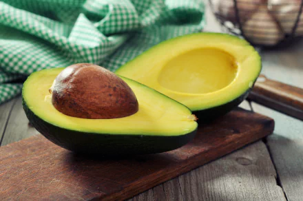 A close-up of a halved avocado on a wooden cutting board, showcasing its creamy flesh and pit, complemented by a green checkered cloth in the background. 4K Ultra HD desktop wallpaper.