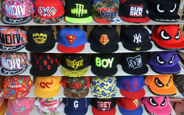 Colorful urban cap display: rows of logo-branded snapback hats in bold street style, vibrant colors on a man-made store shelf — 4K Ultra HD PC desktop wallpaper/background.