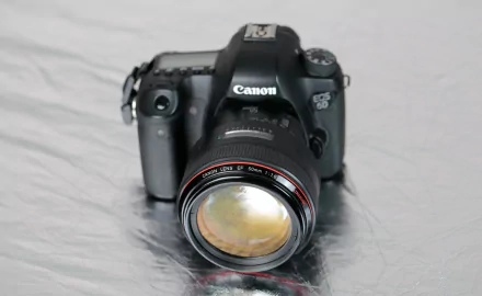 Close-up of a Canon DSLR with a prominent lens on a reflective surface, man-made camera detailed shot — HD PC desktop wallpaper/background.
