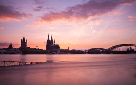 A stunning view of Hohenzollern Bridge over the river in Cologne, Germany, showcases beautiful morning light illuminating the city's architecture and the majestic cathedral.