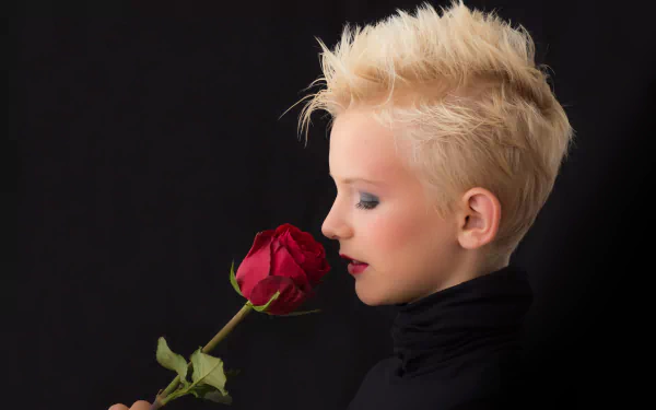 Blonde woman with bold makeup and red lipstick holding a red rose close to her face against a black background in 4K Ultra HD.