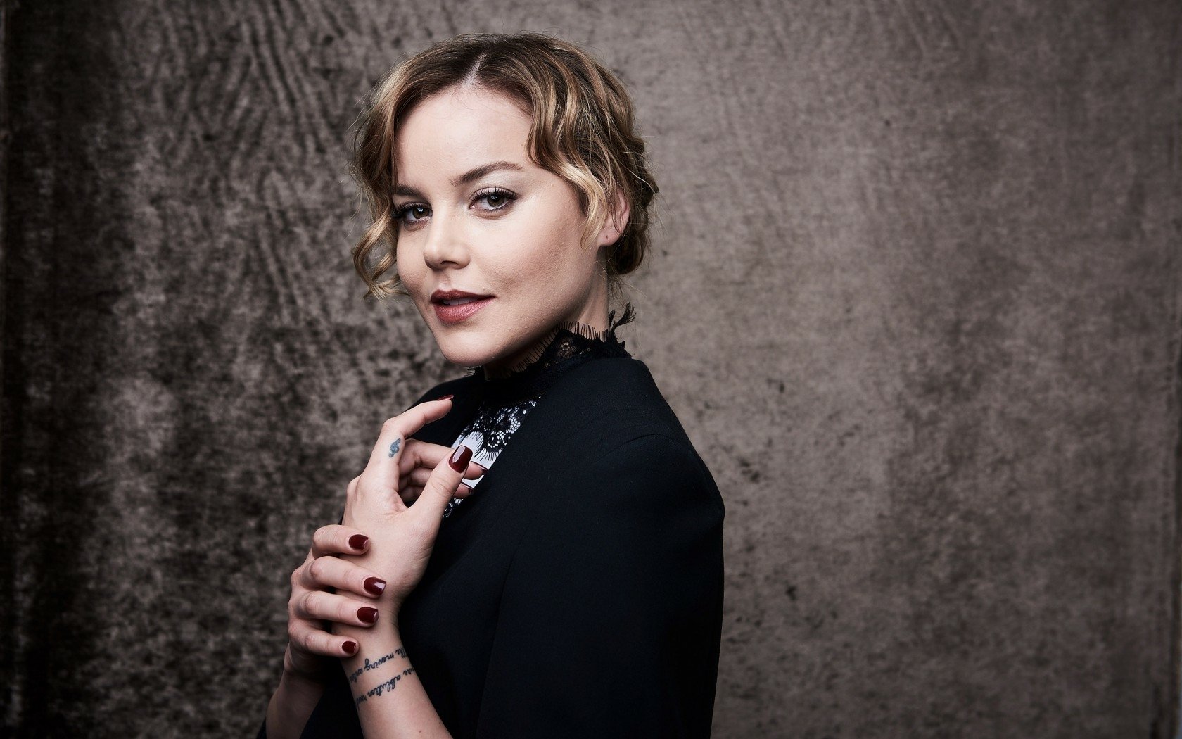 Blonde actress and celebrity in a poised portrait against a textured gray backdrop, hands near collar — HD PC desktop wallpaper.