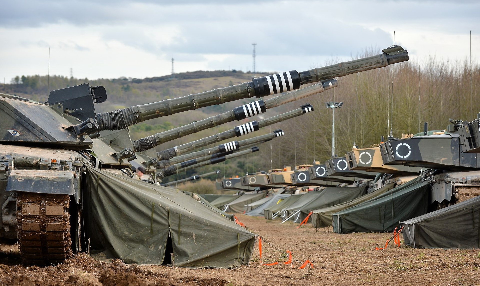 HD PC desktop wallpaper showing a row of Challenger 2 main battle tanks with raised guns at a muddy military encampment beneath a cloudy sky.