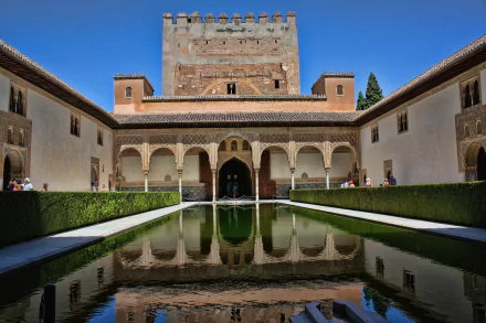 4K Ultra HD image of the Alhambra in Granada, Spain, showcasing its historic architecture and serene reflection in a central pool under a clear blue sky.