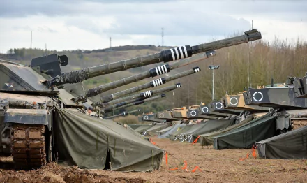 HD PC desktop wallpaper showing a row of Challenger 2 main battle tanks with raised guns at a muddy military encampment beneath a cloudy sky.