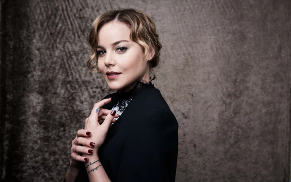 Blonde actress and celebrity in a poised portrait against a textured gray backdrop, hands near collar — HD PC desktop wallpaper.