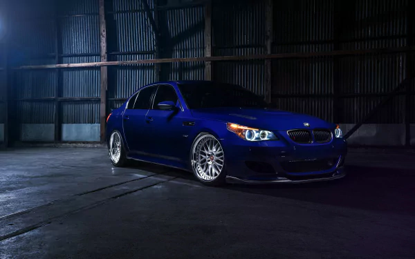 HD desktop wallpaper featuring a sleek blue BMW M5 car parked inside a dimly lit industrial garage, showcasing the vehicle’s sharp design and sporty elegance.