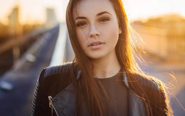 HD desktop wallpaper featuring a close-up portrait of a woman model with long hair, wearing a black leather jacket, bathed in warm golden sunlight.