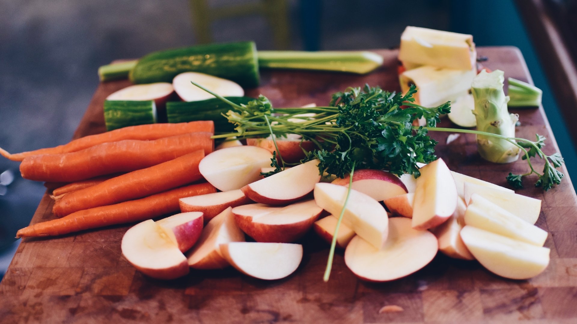 A vibrant 4K Ultra HD wallpaper featuring fresh apples, broccoli, cucumber, parsley, and carrots arranged on a wooden surface showcasing colorful fruits and vegetables.