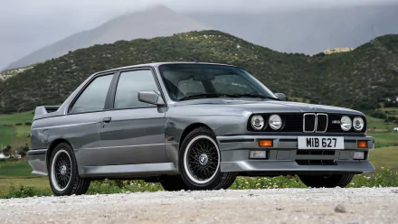 HD PC desktop wallpaper featuring a classic BMW 3 Series parked on a gravel road with mountainous scenery in the background.
