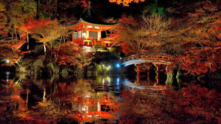 A serene autumn scene at Daigo-ji Japanese garden featuring a lit pagoda, vibrant fall trees, and their reflection in a calm pond beneath an arched wooden bridge.