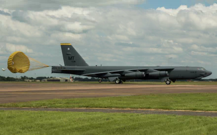 A Boeing B-52 Stratofortress bomber taxiing on a runway, featuring a deployed parachute and a backdrop of cloudy skies, captured in high-definition for a striking military-themed wallpaper.