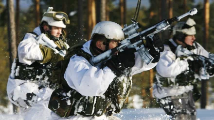 A group of soldiers dressed in winter camouflage, armed with rifles, advance through a snowy landscape in a military exercise. This HD desktop wallpaper captures the intense action and determination.
