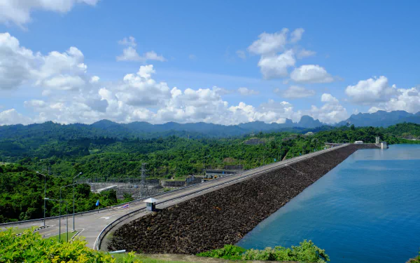 2K Quad HD PC desktop wallpaper/background: man-made dam and roadway beside a blue reservoir under a cloud-dotted sky with green hills.