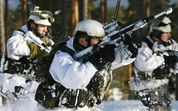 A group of soldiers dressed in winter camouflage, armed with rifles, advance through a snowy landscape in a military exercise. This HD desktop wallpaper captures the intense action and determination.