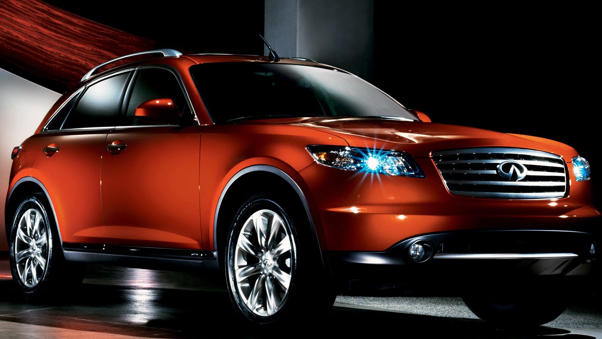 HD PC desktop wallpaper featuring a sleek, orange Infiniti QX70 vehicle with illuminated headlights against a dark background.