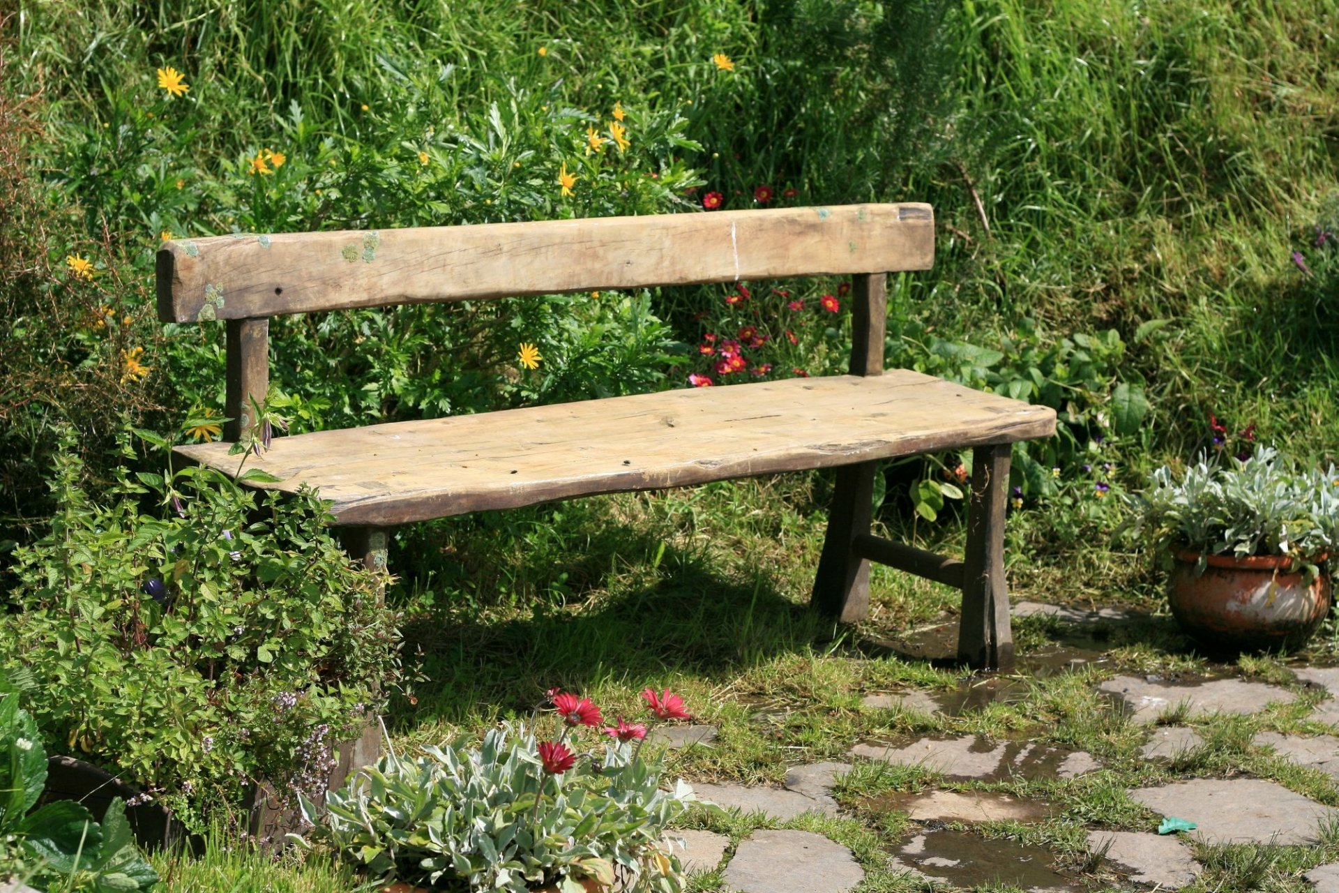 Man-made wooden bench in a Hobbiton garden, surrounded by lush greenery and flowers — HD PC desktop wallpaper background.