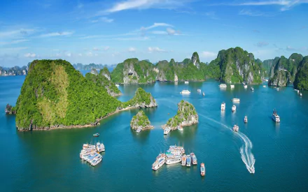 Aerial view of Ha Long Bay in Vietnam, showcasing lush green islands and boats navigating the tranquil waters, creating a stunning tropical landscape for a desktop wallpaper.