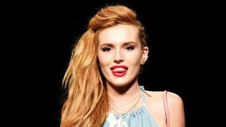 HD desktop wallpaper featuring celebrity Bella Thorne with long red hair styled to one side, wearing a light blue top against a black background.