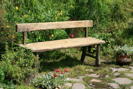Man-made wooden bench in a Hobbiton garden, surrounded by lush greenery and flowers — HD PC desktop wallpaper background.