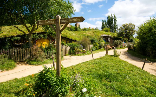 4K Ultra HD image of Hobbiton, a man-made scenic village with lush greenery, winding paths, and rustic signposts under a bright blue sky.