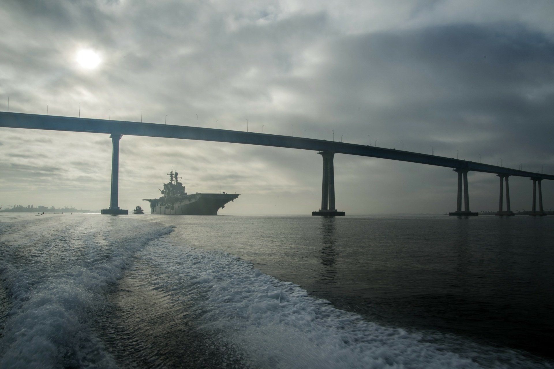 2K Quad HD desktop wallpaper: USS Makin Island (LHD-8) amphibious assault ship steaming beneath the Coronado Bay Bridge at dawn in San Diego.