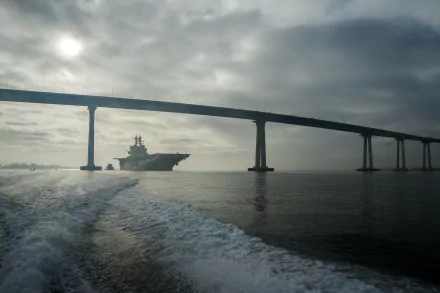 2K Quad HD desktop wallpaper: USS Makin Island (LHD-8) amphibious assault ship steaming beneath the Coronado Bay Bridge at dawn in San Diego.