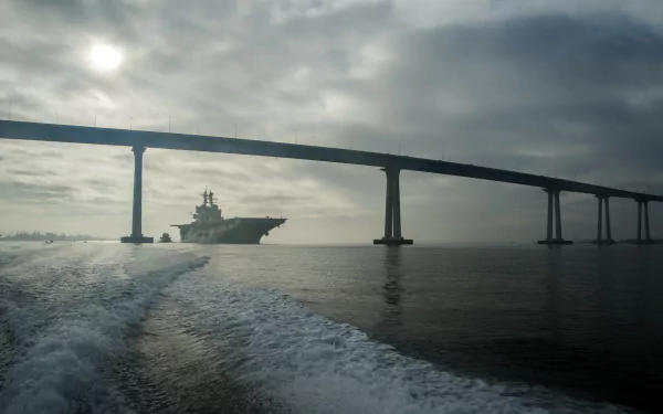 2K Quad HD desktop wallpaper: USS Makin Island (LHD-8) amphibious assault ship steaming beneath the Coronado Bay Bridge at dawn in San Diego.