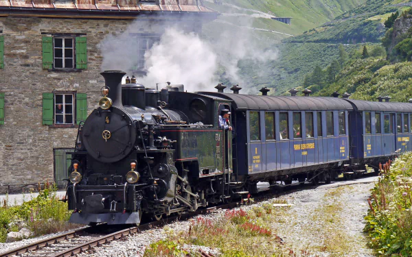 Steam locomotive train vehicle in Switzerland steaming through an alpine valley with vintage passenger cars — 2K Quad HD PC desktop wallpaper background.