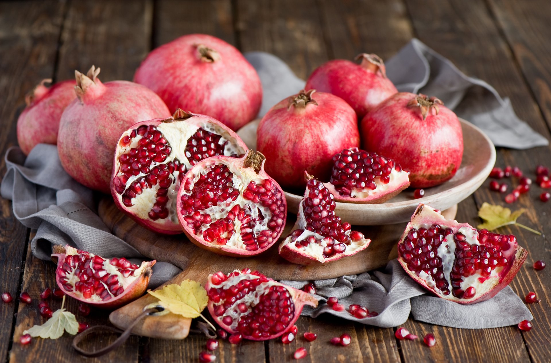 HD desktop wallpaper featuring a still life of ripe pomegranates and scattered seeds on a wooden surface with a gray cloth, highlighting vibrant fruit textures.