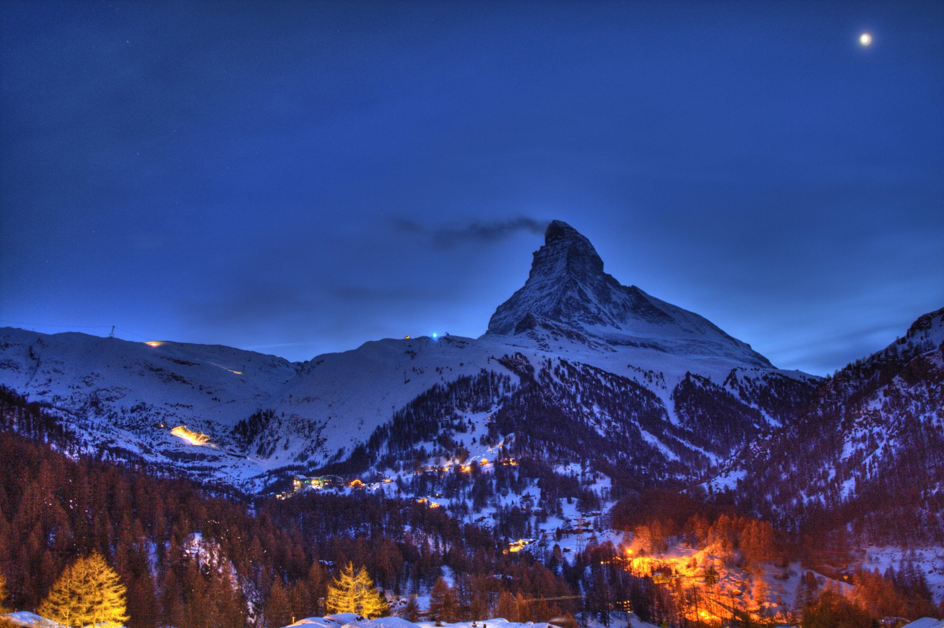 HD desktop wallpaper showcasing the snow-covered Matterhorn mountain under a twilight sky with a glowing star and illuminated village lights below.