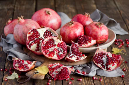 HD desktop wallpaper featuring a still life of ripe pomegranates and scattered seeds on a wooden surface with a gray cloth, highlighting vibrant fruit textures.