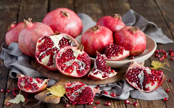 HD desktop wallpaper featuring a still life of ripe pomegranates and scattered seeds on a wooden surface with a gray cloth, highlighting vibrant fruit textures.