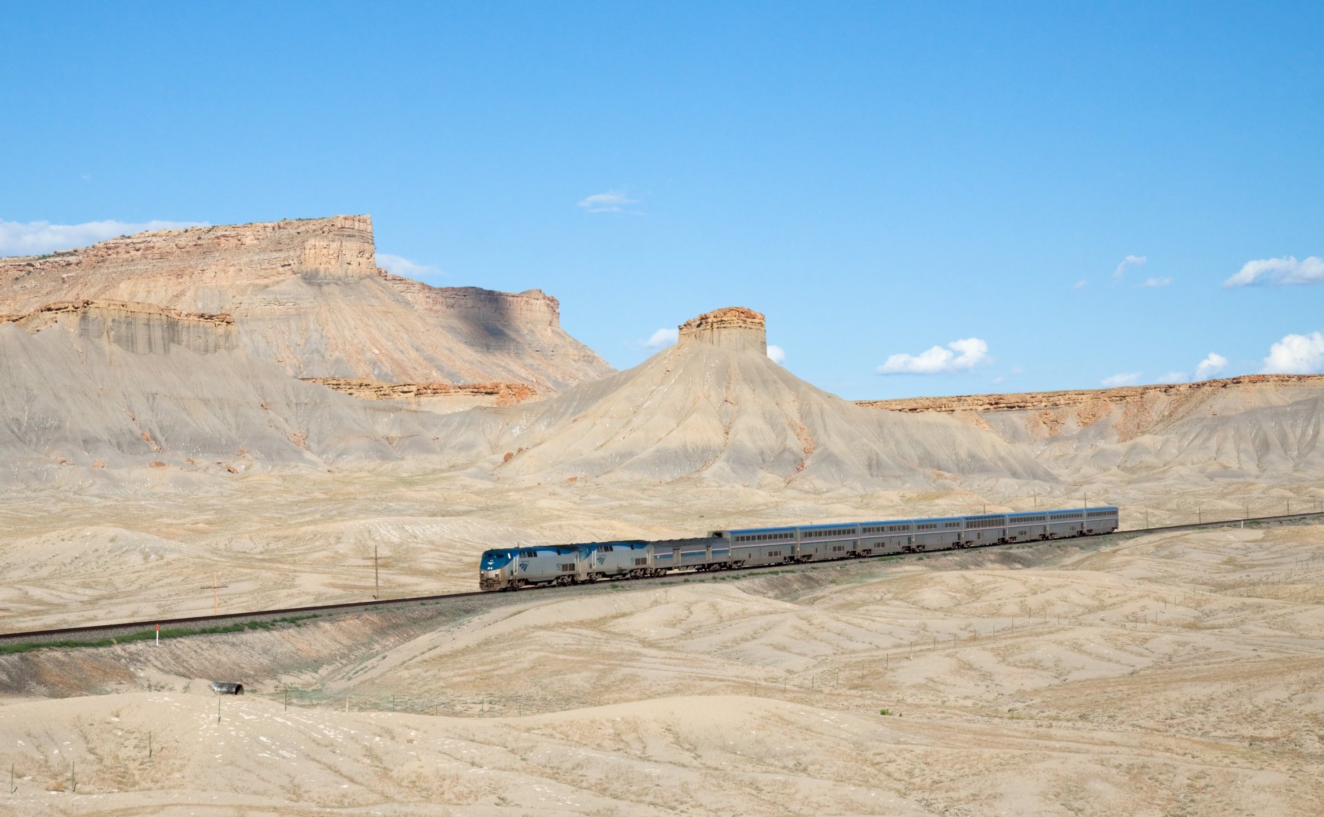 A train travels through a vast desert landscape under a clear blue sky, captured in stunning 4K Ultra HD as a PC desktop wallpaper and background.