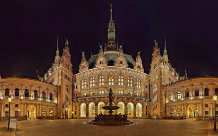 Night view of Hamburg's ornate historic building with a central fountain and statue, showcasing intricate architecture in this HD desktop wallpaper.
