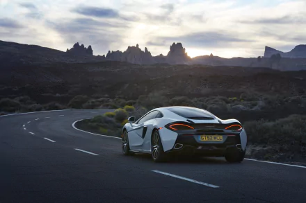 White McLaren 570GT supercar driving on a winding road at sunset, captured in 4K Ultra HD as a stunning PC desktop wallpaper.