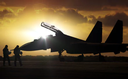 Silhouette of a Sukhoi Su-30 jet fighter at sunset with two military personnel nearby. HD desktop wallpaper.