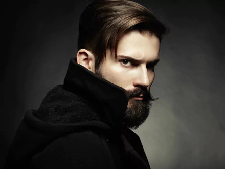 A striking HD wallpaper featuring a man with brown eyes and a full beard, captured in a dramatic pose against a dark background. Ideal for modern desktop aesthetics.