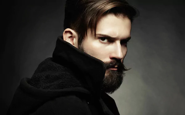 A striking HD wallpaper featuring a man with brown eyes and a full beard, captured in a dramatic pose against a dark background. Ideal for modern desktop aesthetics.