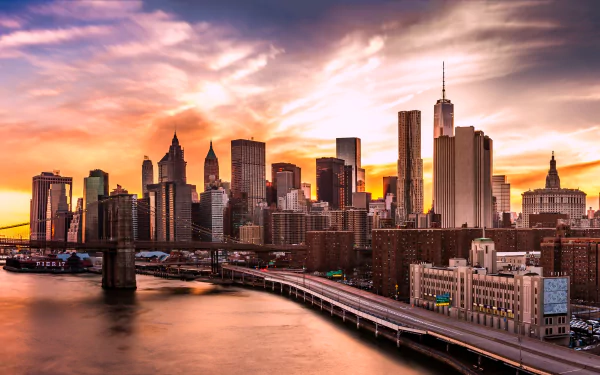 4K Ultra HD desktop wallpaper of the Brooklyn Bridge leading into the Manhattan, New York skyline at sunset, with towering man-made buildings and the waterfront glowing in warm light.