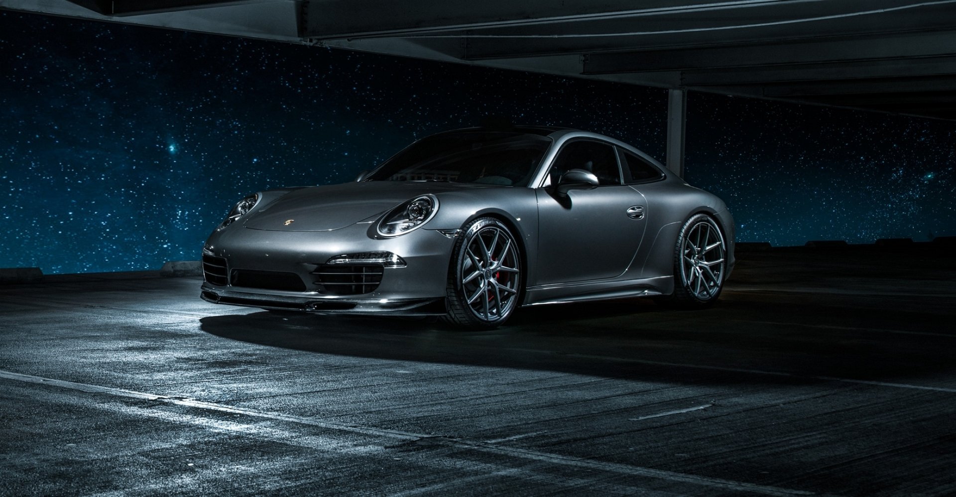 Silver Porsche 911 Carrera 4S parked in a dimly lit space with a starry night sky background, HD desktop wallpaper showcasing the sleek vehicle design.