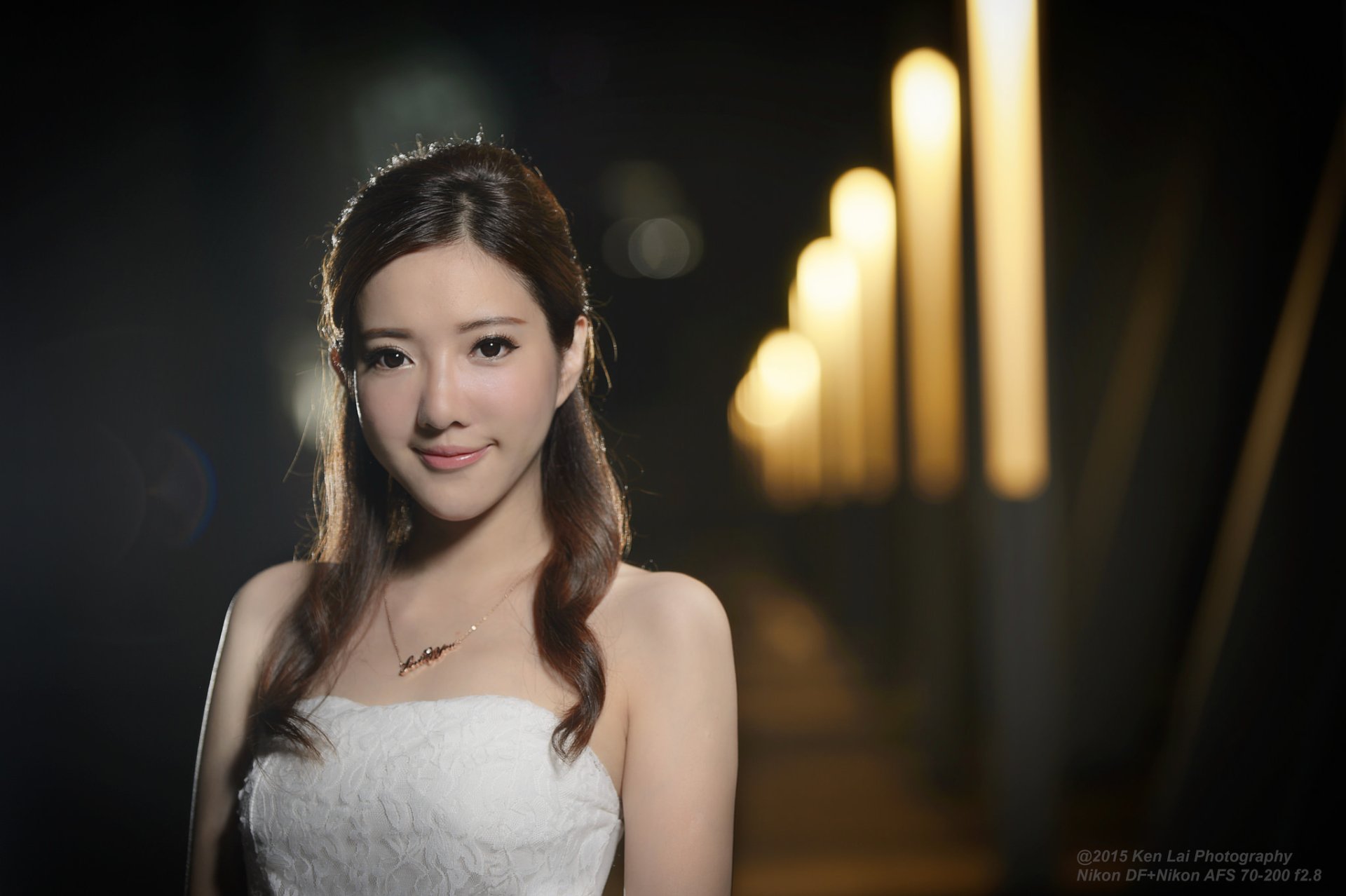 HD PC desktop wallpaper of a smiling woman in a white dress, softly lit against a row of warm, blurred lights.