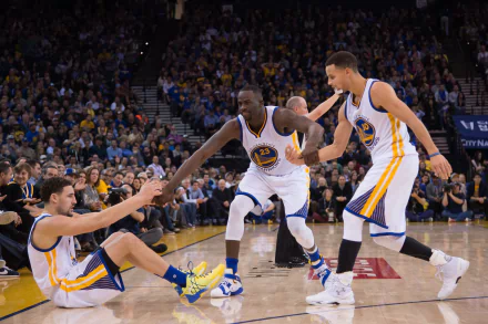 Dynamic moment featuring Golden State Warriors players on the court, as one teammate helps another up during a game. A vibrant sports-themed HD desktop wallpaper.