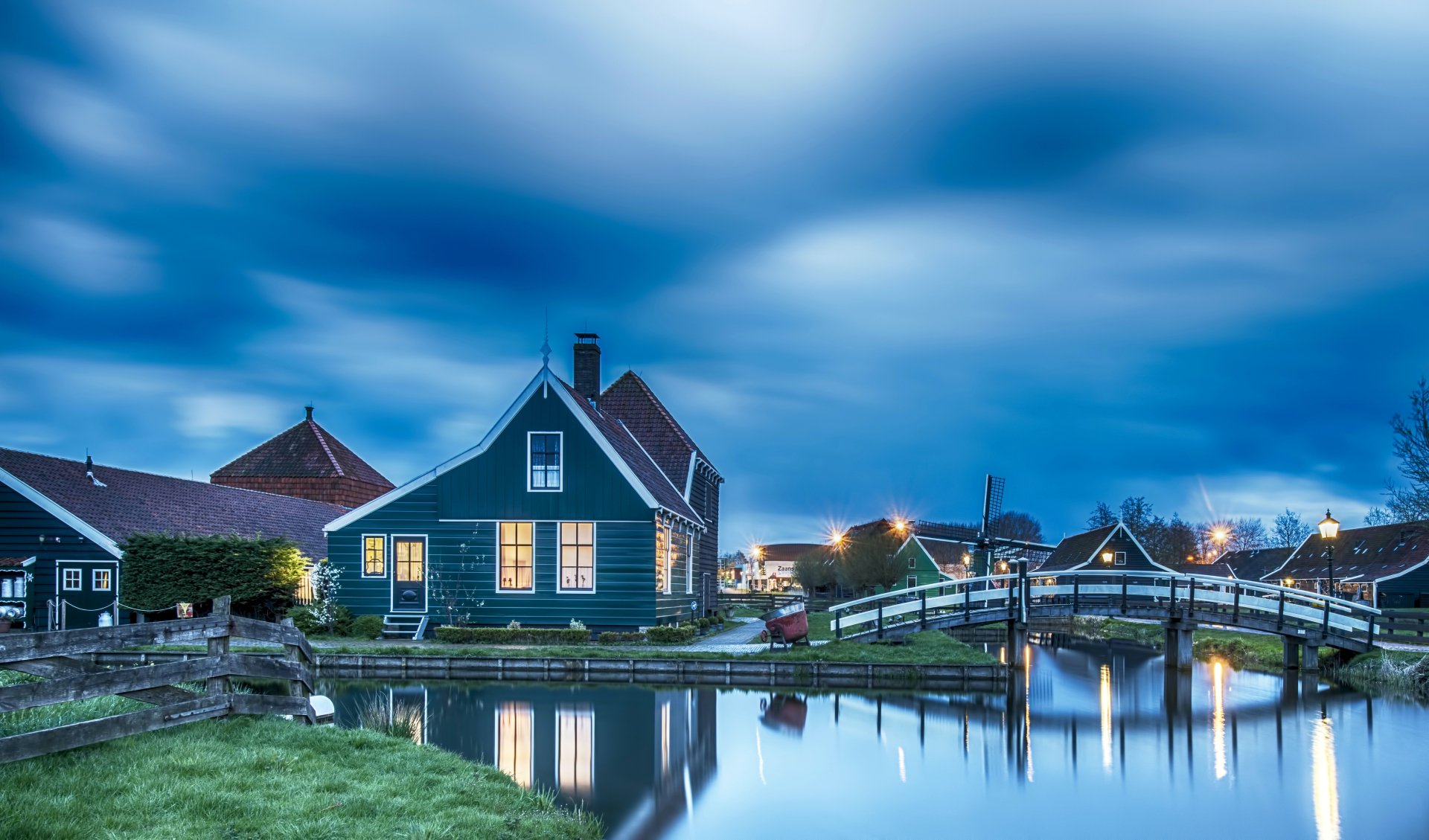 4K Ultra HD PC desktop wallpaper of a small town at dusk: a house by a calm canal with a wooden bridge and other man-made waterfront structures.