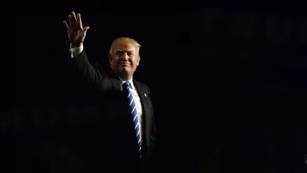HD desktop wallpaper featuring a man in a dark suit, white shirt, and striped tie waving, set against a dimly lit backdrop.