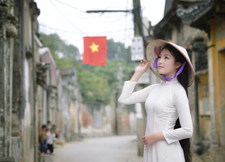 A woman in a traditional Ao Dai and conical hat poses gracefully on a charming street, with a Vietnamese flag in the background, capturing the essence of Vietnamese culture.