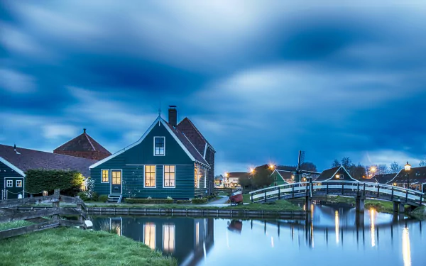 4K Ultra HD PC desktop wallpaper of a small town at dusk: a house by a calm canal with a wooden bridge and other man-made waterfront structures.